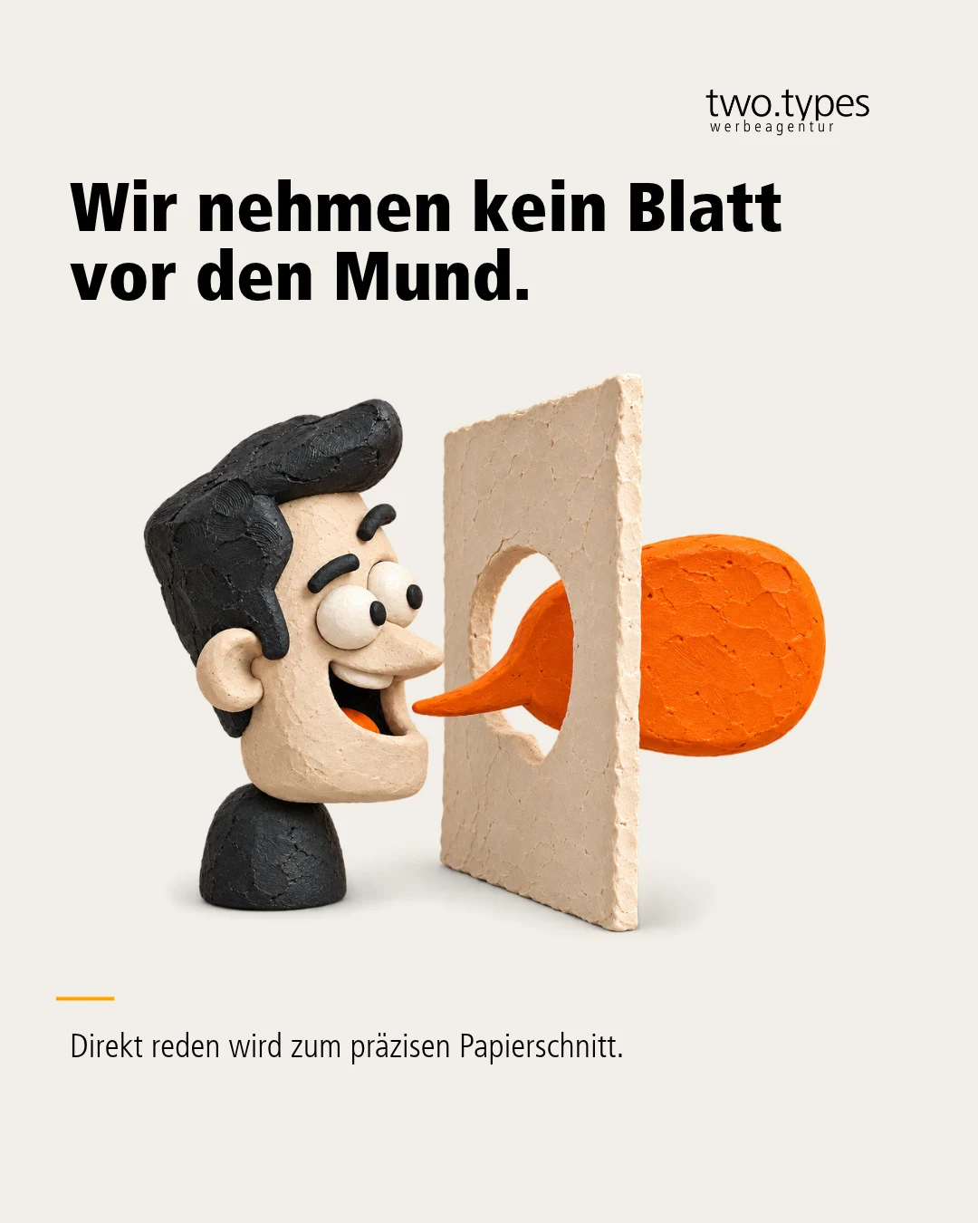 Ein lachender Knetkopf schiebt seine orange Zunge durch den ausgeschnittenen Mund eines Papierblatts.
