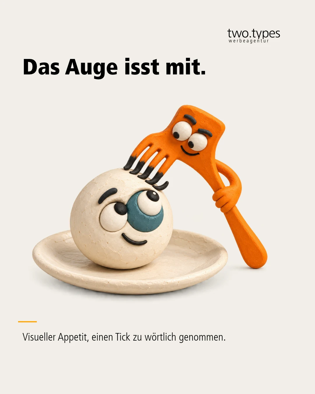 Eine orange Gabel beugt sich über einen Augapfel auf einem Teller und blickt ihm in die Pupille.